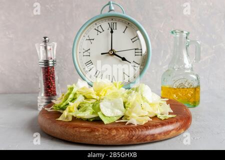 Wecker und Platte mit grünem Eisberg Salat, Olivenöl, intermittiertem Fastenkonzept, ketogener Ernährung, Gewichtsverlust Stockfoto