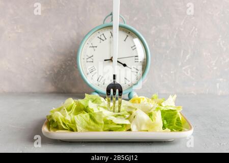 Wecker und Platte mit grünem Eisbergsalat, intermittiertem Fastenkonzept, ketogener Ernährung, Gewichtsverlust Stockfoto