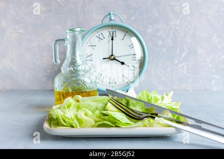 Wecker und Platte mit grünem Eisberg Salat, Olivenöl, intermittiertem Fastenkonzept, ketogener Ernährung, Gewichtsverlust Stockfoto