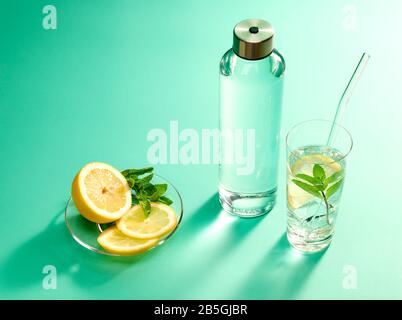 Wiederverwendbare Glasflasche mit Zitrone, Pfefferminze und Glas auf minzgrünem Hintergrund Stockfoto