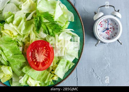 Wecker und Platte mit grünem Eisberg Salat, intermittiertem Fastenkonzept, Ernährung, Gewichtsverlust Stockfoto