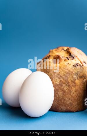 Osterkuchen und drei weiße Hühnereier auf klassischem blauem Hintergrund in der Nahaufnahme. Nahaufnahme von Osterkuchen und Eiern auf einem Stockfoto