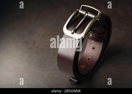 Modischer, brauner Gürtel aus echtem Leder mit einer hellen Metallschnalle auf dunklem Hintergrund. Echtes Leder, handgefertigt. Nahaufnahme Stockfoto