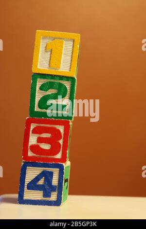 Vertikaler Stapel von farbigen Holzspielzeugblöcken aus Alphabet auf orangefarbenem Hintergrund Stockfoto