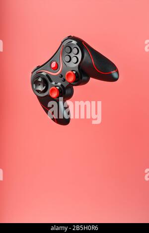 Ein schwarzer Joystick-Gamecontroller schwebt isoliert auf einem rosafarbenen Hintergrund. Interaktive Unterhaltung. Konzept. Freier Speicherplatz. Gerät zur Steuerung und Steuerung t Stockfoto