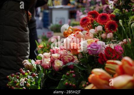 Düsterer Moody-Ton. Ausgewählte Fokusansicht in hellorange, pink und weiß Blumenstrauß mit blühenden Rosen vor Blumenladen auf dem Freiluftmarkt in Europa. Stockfoto