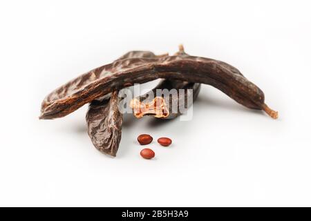 Karob-Karob-Früchte und Samen auf weißem Hintergrund. Isolieren. Biobohnen, eine gesunde Alternative zum Kakao. Stockfoto