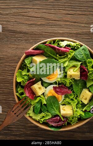 Gesunder Salat mit Eiern und Käse auf Holztischgrund. Gesunde Mahlzeit. Stockfoto