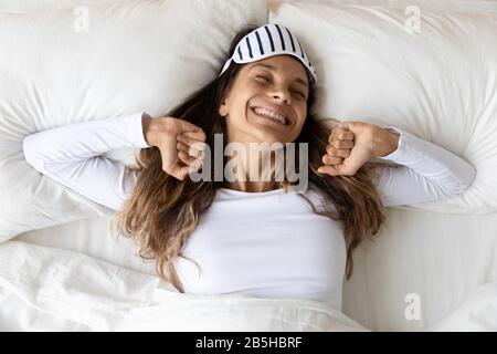 Glückliches tausendjähriges Mädchen, das sich im Schlafzimmer ausdehnt, erwacht Stockfoto