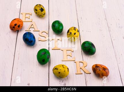 Mehrfarbige Osterquageleier und die Aufschrift Ostern auf weißem Holzhintergrund. Stockfoto