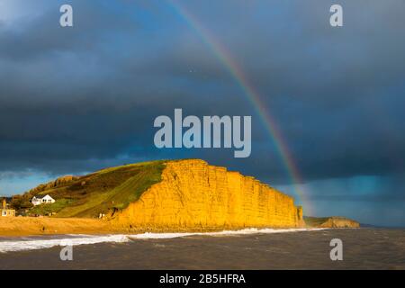 West Bay, Dorset, Großbritannien. März 2020. Wetter in Großbritannien. Ein Regenbogenbogen über den Klippen, der am späten Nachmittag bei Sonnenschein in der West Bay in Dorset als dunkle Duschwolke beleuchtet wird, geht über. Bildnachweis: Graham Hunt/Alamy Live News Stockfoto