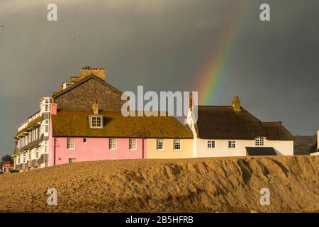 West Bay, Dorset, Großbritannien. März 2020. Wetter in Großbritannien. Eine Regenbogenbögen über einigen Cottages am Meer, die am späten Nachmittag bei der Sonne in der West Bay in Dorset beleuchtet werden, während eine dunkle Duschwolke über die Küste führt. Bildnachweis: Graham Hunt/Alamy Live News Stockfoto