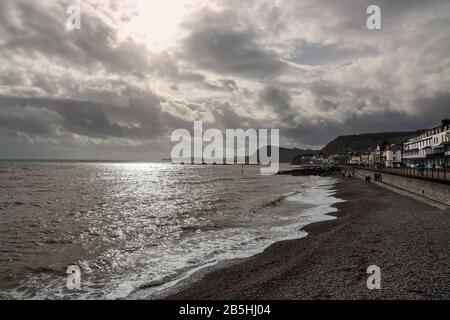 Regency-Gebäude sämen die Esplanade am Kanalort Sidmouth in Devon. Das Sonnenlicht funkelt auf dem Meer und lappt am Kieselstrand, ohne dass es zu Wasser kommt Stockfoto