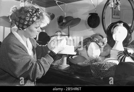In den 1980er Jahren zeigt das Foto eine Hutmacherin oder Mühlerin, die in ihrem Handwerk sitzt, mit einer Tischausstellung ihrer Kopfbekleidungskreationen in England, Großbritannien. Die Mühlerei wird oft von unabhängigen Arbeitern betrieben, Einzelhändlern, die die Design- und kreativen Aspekte der maßgeschneiderten Hutmacherei genießen. Stockfoto