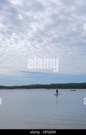 Foz Do Arelho, Portugal, 8. März 2020 - ältere Frau auf einem SUP-Paddlebarden. Mit schwarzem und pinkfarbenem Neoprenanzug Stockfoto