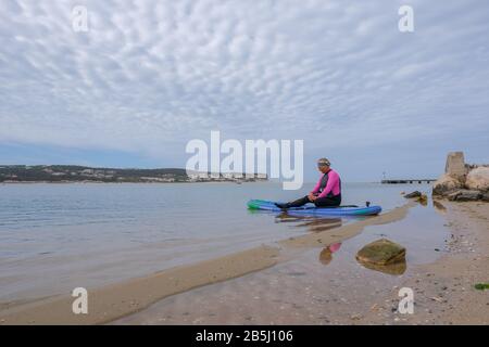 Foz Do Arelho, Portugal, 8. März 2020 - eine ältere Frau, die auf einem SUP-Paddleboard sitzt Stockfoto