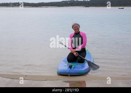 Foz Do Arelho, Portugal, 8. März 2020 - eine ältere Frau, die auf einem SUP-Paddleboard sitzt Stockfoto