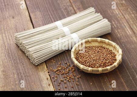 Gebündelte getrocknete Soba (Nudeln mit japanischem Buchweizen) und Buchweizensamen auf Holzgrund Stockfoto