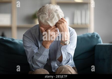 Unglücklicher alter Mann sitzt auf der Couch weinend sehnsüchtiges Stockfoto