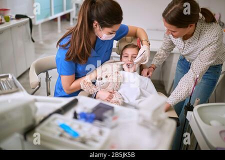 Der Zahnarzt untersucht die Zähne des Kindes mit Spiegel Stockfoto