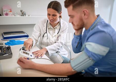 Der junge weibliche Arzt misst den Blutdruck zum Patienten Stockfoto