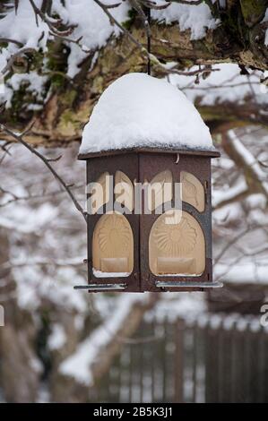 Dekorative Außenlaterne im Schnee ist ein Messingobjekt, das an einem Baum hängt, der im Winter mit vielen Zentimeter frisch gefallenem Schnee bedeckt ist. Stockfoto