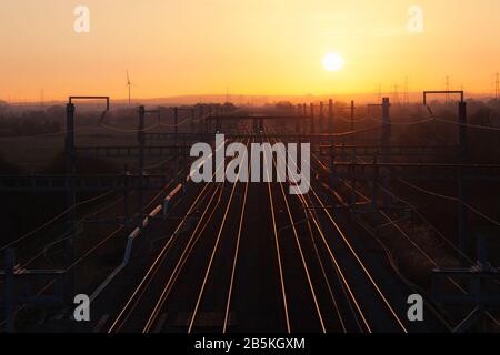 Blick auf die 4-spurige große westliche Hauptbahnstrecke bei Coedkernew mit untergehenden Sonnen- und Grünbahnsignalen Stockfoto