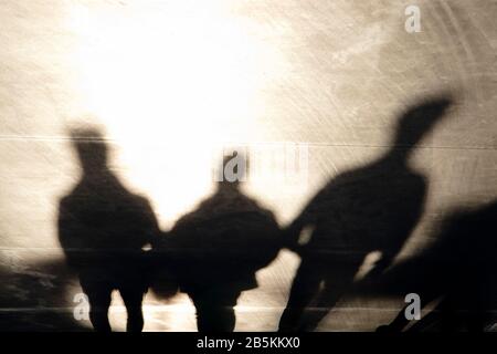 Schatten Silhouetten von drei mysteriösen Männern, die auf der Promenade bei Sonnenuntergang in Sepia schwarz und weiß laufen Stockfoto