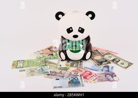 Panda Bear Piggy Bank umgeben von verschiedenen West- und Ostweltwährungen Stockfoto