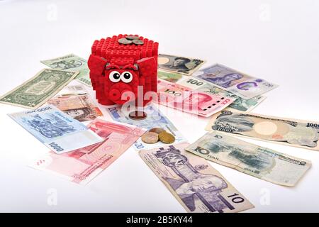 Montierte rote lego Piggy Bank umgeben von verschiedenen Währungen Papierscheine und Münzen aus der ganzen Welt Stockfoto