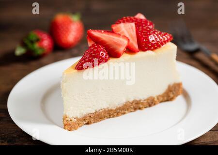 Käsekuchen mit Erdbeeren auf dem Teller, Holztischhintergrund Stockfoto