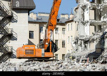 Nahaufnahme eines speziellen Hydraulikbagger-Destroyer während des Betriebs, Ruinen eines Gebäudes auf dem Hintergrund. Extrem hohe Abbruchausrüstung. Stockfoto