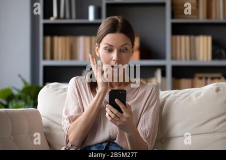 Schockierte junge Brunette-Frau beim Blick auf den Smartphone-Bildschirm. Stockfoto