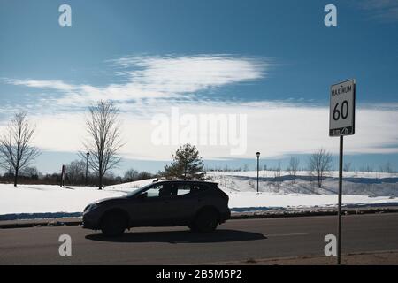 Ein Auto fährt auf der Bronson Avenue in südlicher Richtung unter einem kalten, winterlichen, pulverblauen Himmel und bläulichen weißen Wolken. Ottawa, Ontario, Kanada. Stockfoto