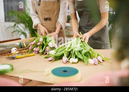 Zugeschnittenes Porträt zweier junger Frauen, die Blumenkompositionen und Tulpensträuße für die Frühlingssaison arrangieren, während sie im Blumenladen arbeiten und Platz für Kopien schaffen Stockfoto