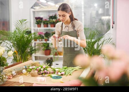 Taille hoch Portrait der kreativen jungen Frau, die ein Smartphone-Foto von Tulpenblumen bei der Arbeit im Blumenladen und im Kopierraum aufgenommen hat Stockfoto