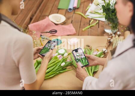 Hochwinkelansicht bei zwei Frauen, die ein Smartphone-Foto von Tulpenblumen machen, während sie im Blumenladen arbeiten, Kopierraum Stockfoto