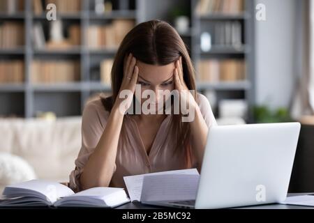 Betonte junge Frau, die den Kopf in den Händen hält und sich verzweifelt fühlt. Stockfoto