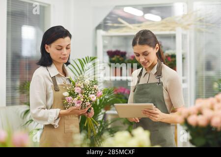 Taille hoch Portrait von zwei weiblichen Floristen, die Blumensträuße arrangieren und digitale Tablette verwenden, während sie in Blumenladen arbeiten, Kopierraum Stockfoto