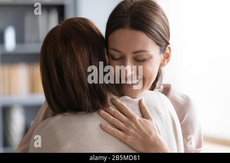 Liebevolle junge Frau, die die brünette Mutter mittleren Alters umarmte. Stockfoto