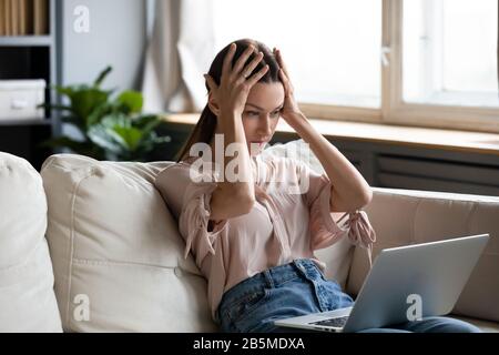 Nervös frustrierte junge Frau, die auf den Computerbildschirm blickt. Stockfoto