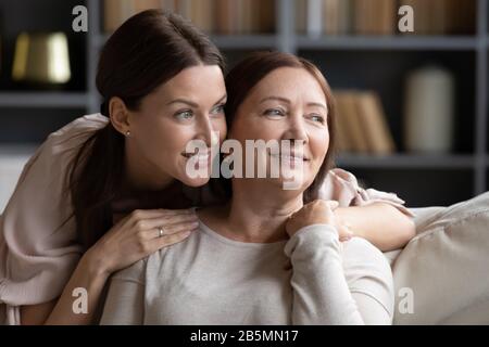 Verträumte Frauen mit zwei Generationen, die sich zu Hause entspannen. Stockfoto