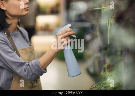 Zugeschnittenes Porträt der jungen Frau, die Pflanzen gießen, während sie in Blumenladen arbeiten, Kopierer Stockfoto