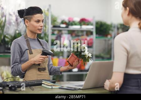 Seitenansicht Porträt der modernen jungen Frau, die Blumen in Blumenladen und Barcode scannen, Kopierer Stockfoto
