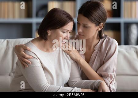 Mitfühlende Frau, die die Schulter der unglücklich gestressten Mutter mittleren Alters umarmte. Stockfoto