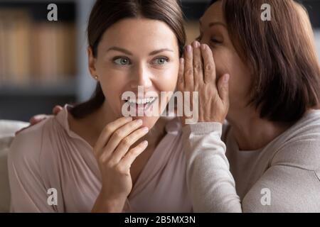 Glückliche Mutter mittleren Alters flüstert Tratsch an Erwachsene Tochter. Stockfoto