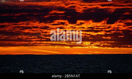 Wolken, die von der untergehenden Sonne über dem blauen Wasser der Ostsee erleuchtet werden. Stockfoto