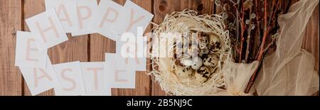 Flache Laienzusammensetzung aus Wachteleiern und Karte mit Text Happy Easter auf Holztisch. Draufsicht. Stockfoto
