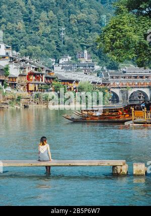 Frau, die in Fenghuang, der alten Stadt, in China, über dem Flusswasser Li sitzt Stockfoto