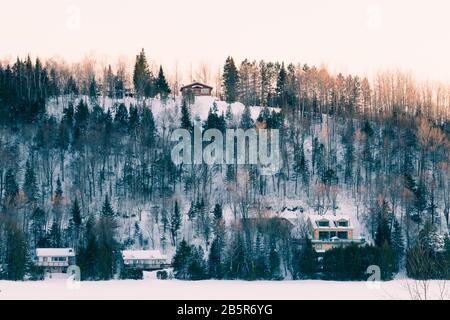 Winteruntergang auf dem Hügel - Landschaft mit Bäumen, Cottages und Schnee in Laurentides, Quebec, Kanada Stockfoto